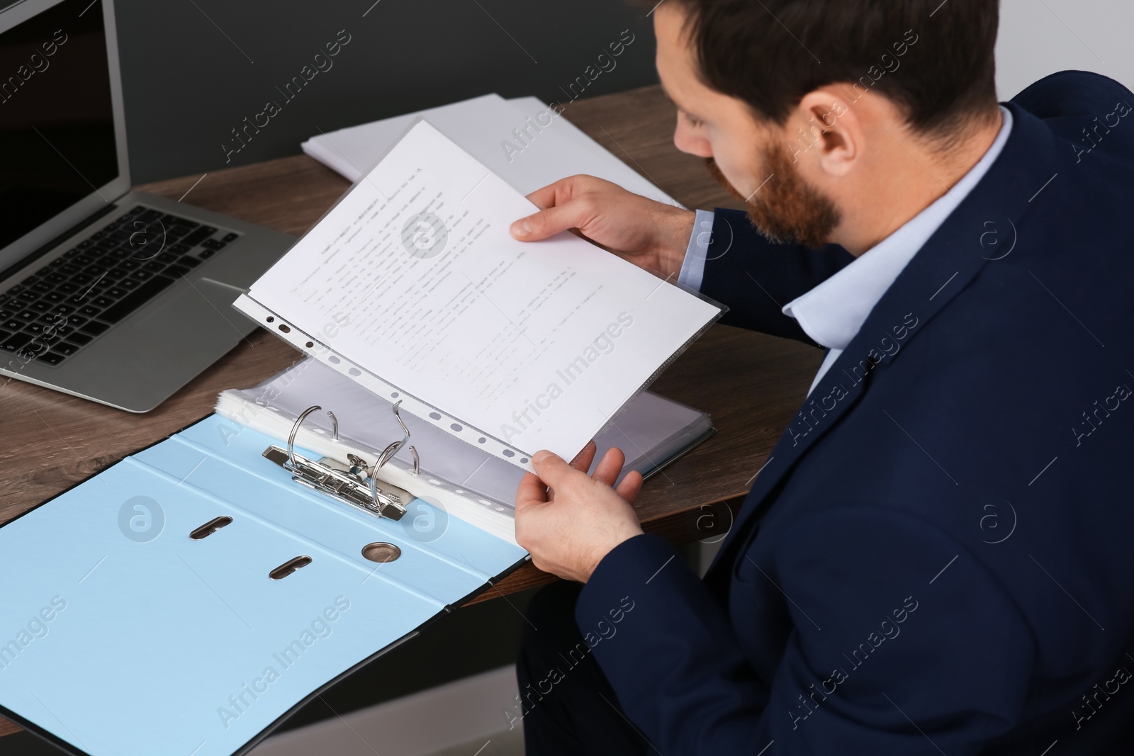 Photo of Businessman putting document into file folder at wooden table in office