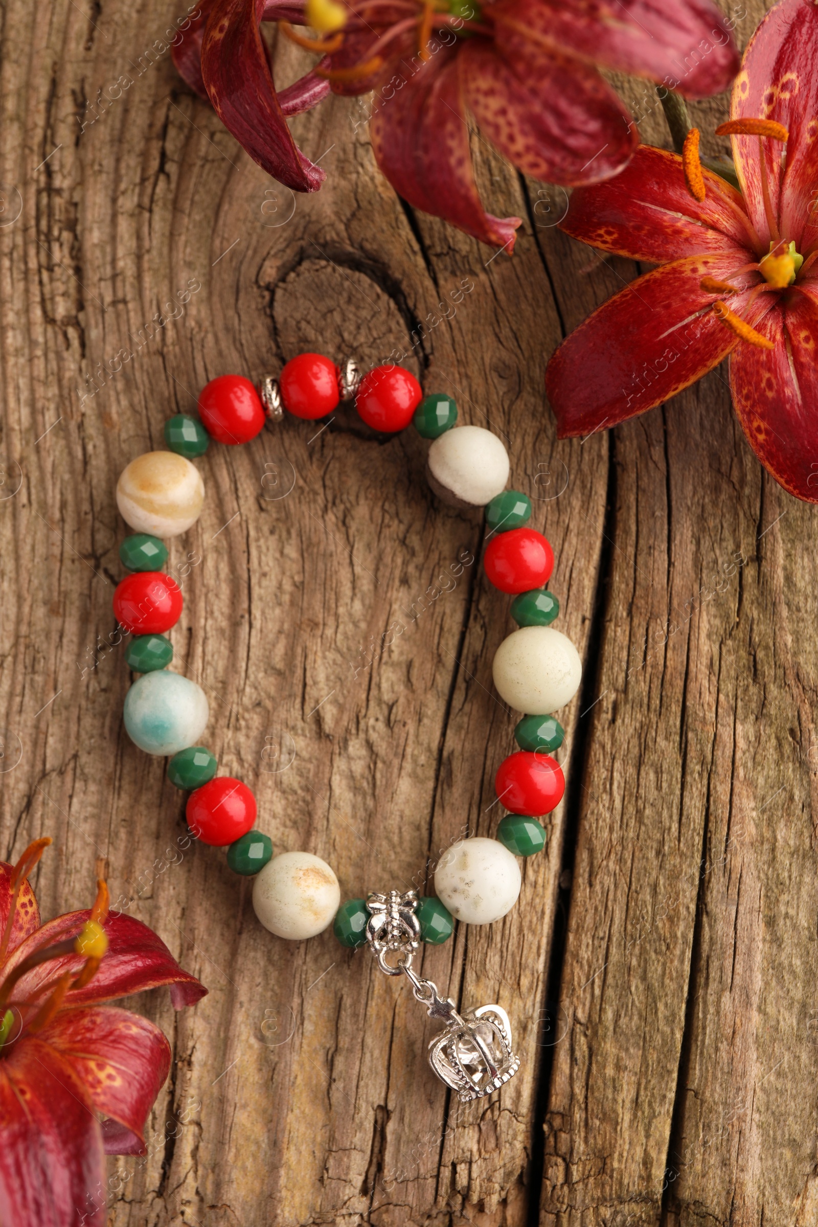 Photo of Beautiful bracelet with gemstones and lily flowers on wooden surface, flat lay