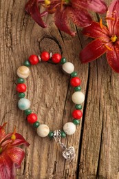 Beautiful bracelet with gemstones and lily flowers on wooden surface, flat lay