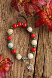 Photo of Beautiful bracelet with gemstones and lily flowers on wooden surface, flat lay