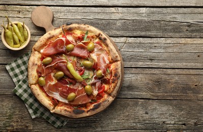 Tasty pizza with cured ham, olives, sun-dried tomato and peppers on wooden table, top view. Space for text