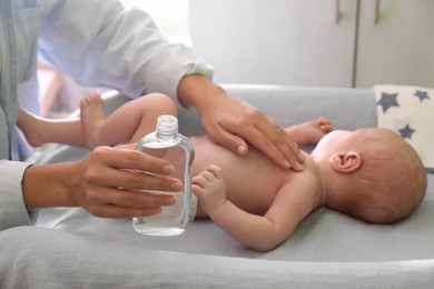 Mother with bottle of massage oil near baby on changing table indoors, closeup