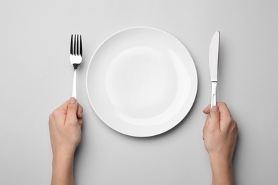 Photo of Woman with fork, knife and empty plate on grey background, top view