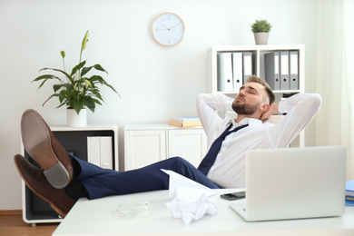Photo of Lazy young man wasting time at table in office