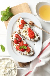 Photo of Delicious ricotta bruschettas with strawberry, mint and pistachios served with honey on white wooden table, flat lay