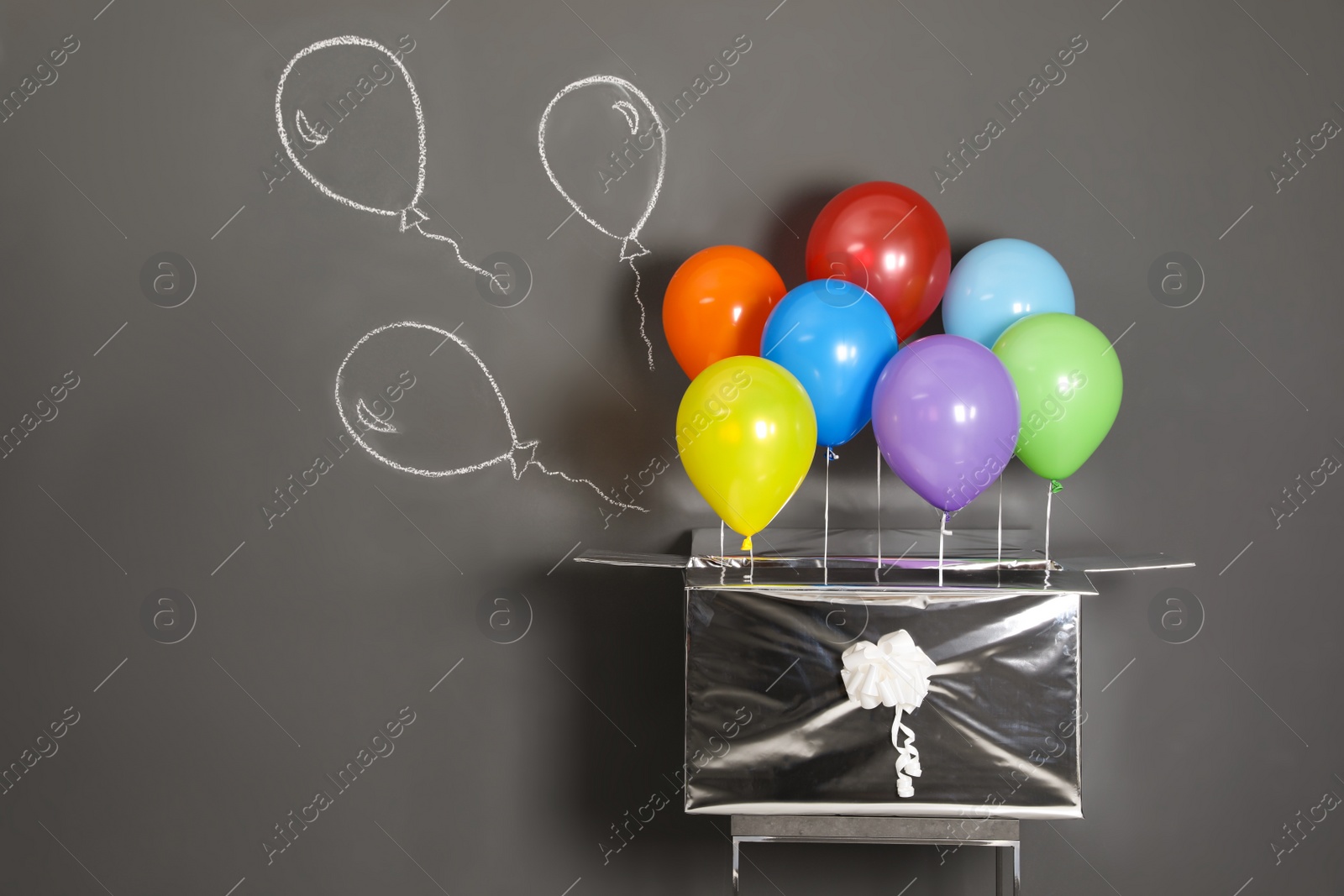 Photo of Gift box with bright air balloons and chalk drawing on grey background