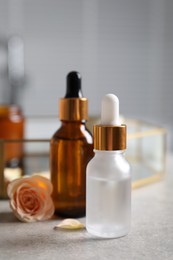 Bottles of cosmetic serum and beautiful flower on gray table, closeup