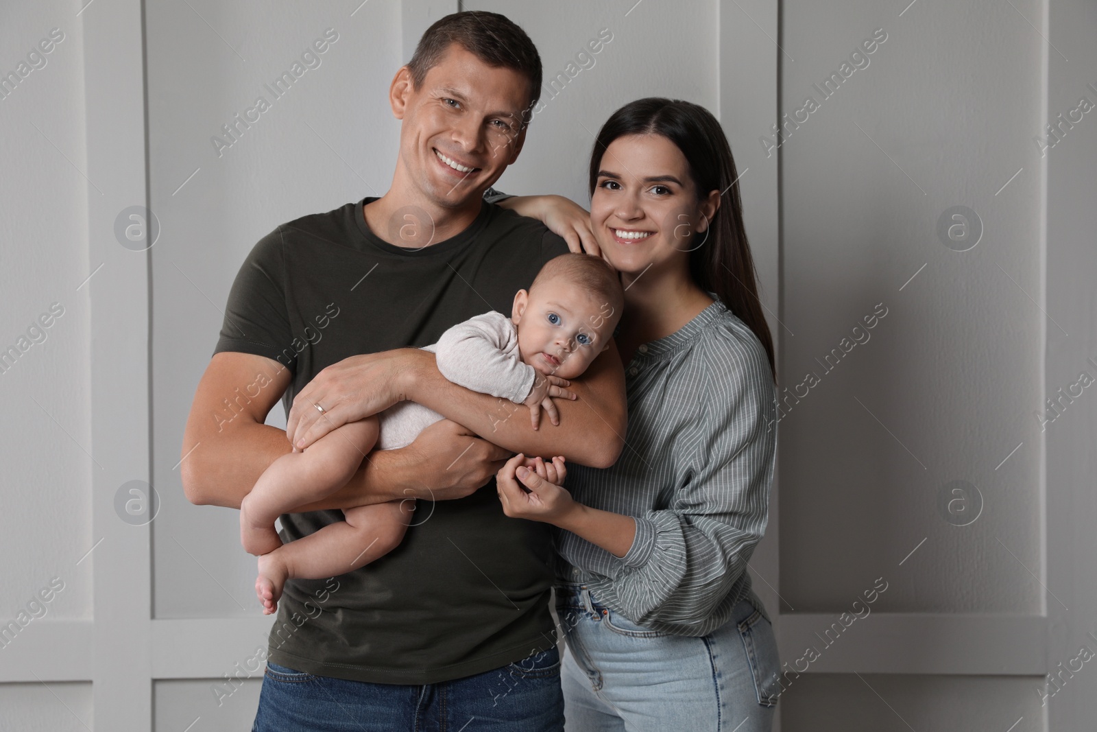 Photo of Happy family. Couple with their cute baby near light wall