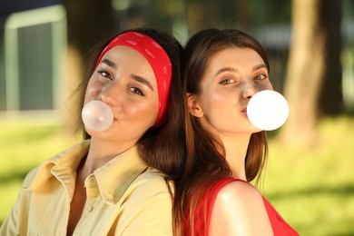 Beautiful young women blowing bubble gums in park