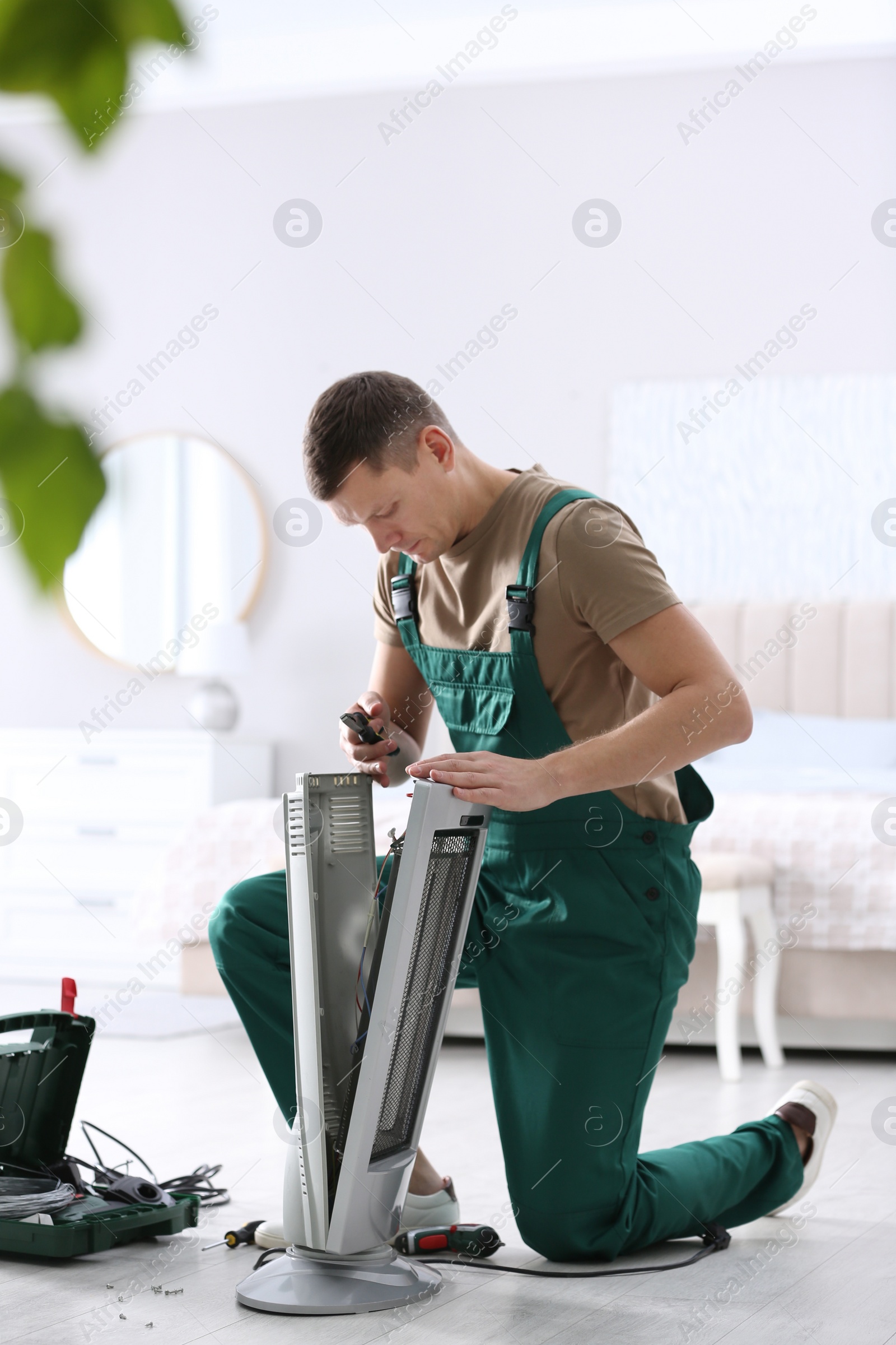 Photo of Professional technician repairing electric ultrared heater with pliers indoors