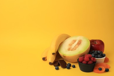 Photo of Delicious fruits, berries and pieces of chocolate on yellow background, space for text