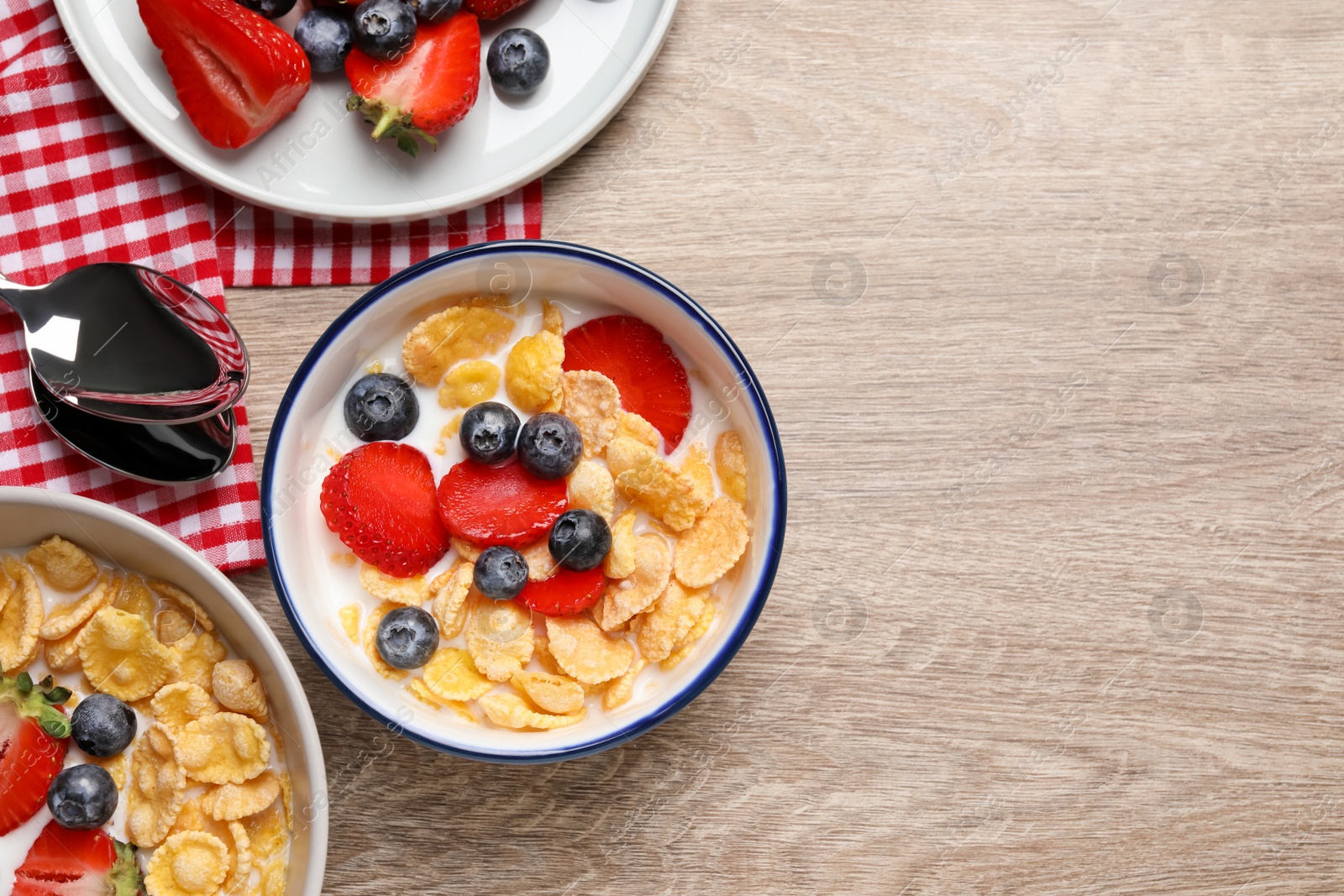 Photo of Delicious crispy cornflakes with milk and fresh berries on wooden table, flat lay. Space for text