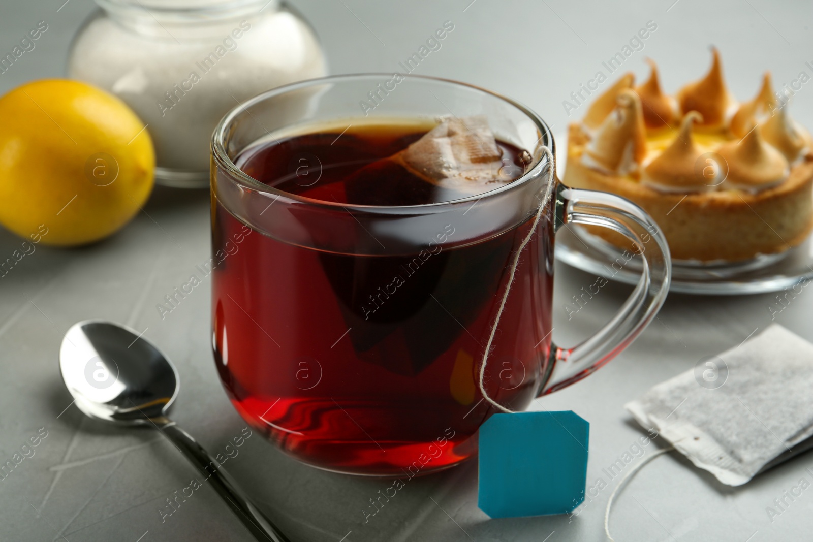 Photo of Tea bag in glass cup of hot water on grey table