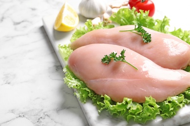 Photo of Board with raw chicken breasts and lettuce on marble table. Space for text