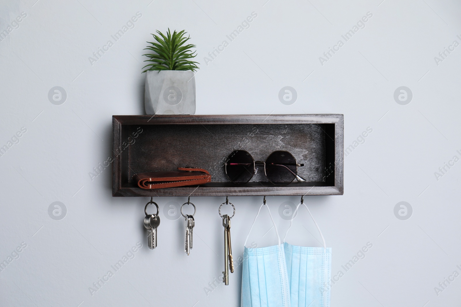 Photo of Wooden hanger for keys with wallet, sunglasses, medical masks and houseplant on white wall