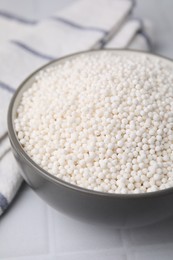 Photo of Tapioca pearls in bowl and towel on white tiled table, closeup