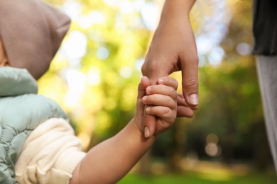 Photo of Daughter holding mother's hand outdoors, closeup. Happy family