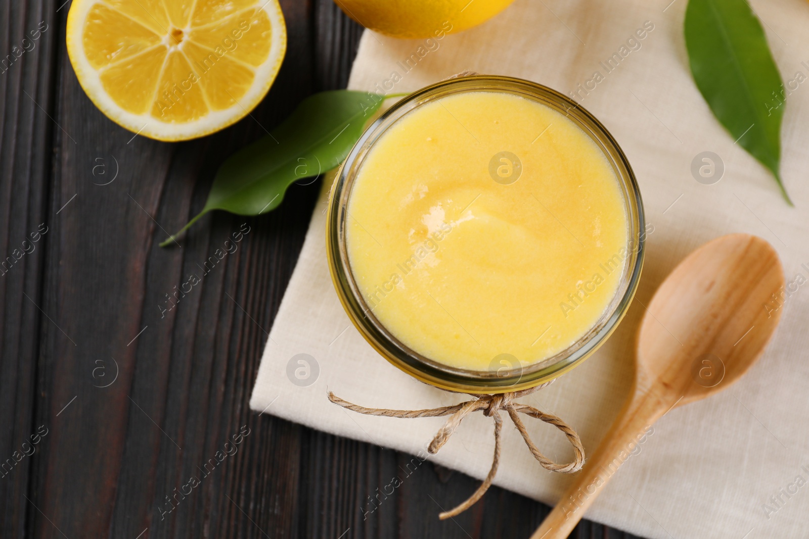 Photo of Delicious lemon curd in bowl, fresh citrus fruit and spoon on wooden table, top view