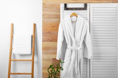 Photo of Fresh white bathrobe hanging on folding screen indoors