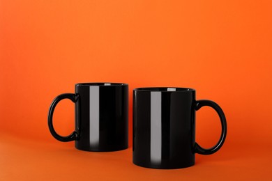Photo of Blank black ceramic mugs on orange background