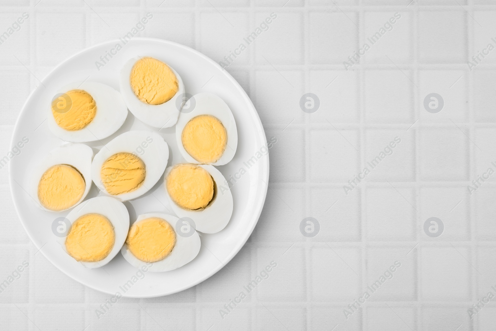 Photo of Fresh hard boiled eggs on white tiled table, top view. Space for text