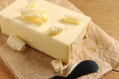 Tasty butter and knife on wooden table, closeup