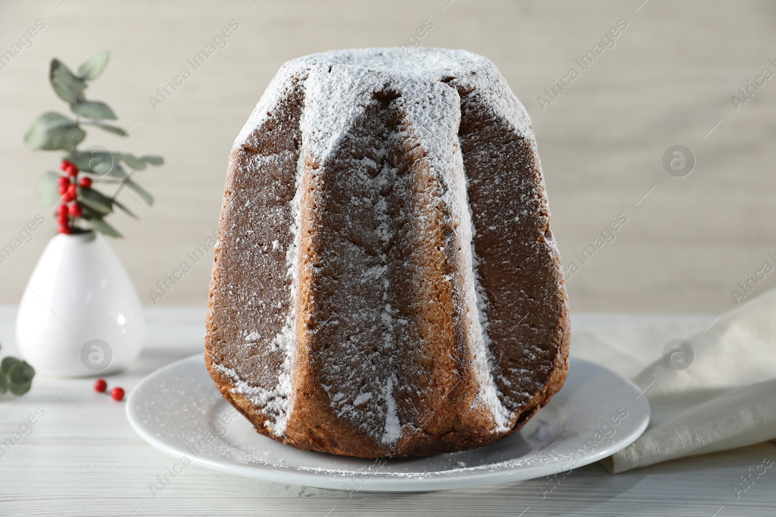 Photo of Delicious Pandoro cake decorated with powdered sugar on white wooden table, closeup. Traditional Italian pastry
