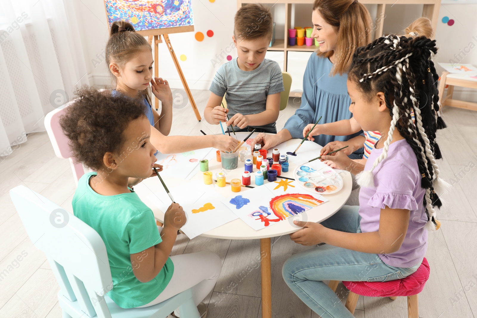 Photo of Children with female teacher at painting lesson indoors