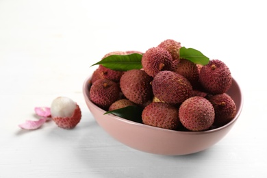 Photo of Fresh ripe lychees in bowl on white wooden table