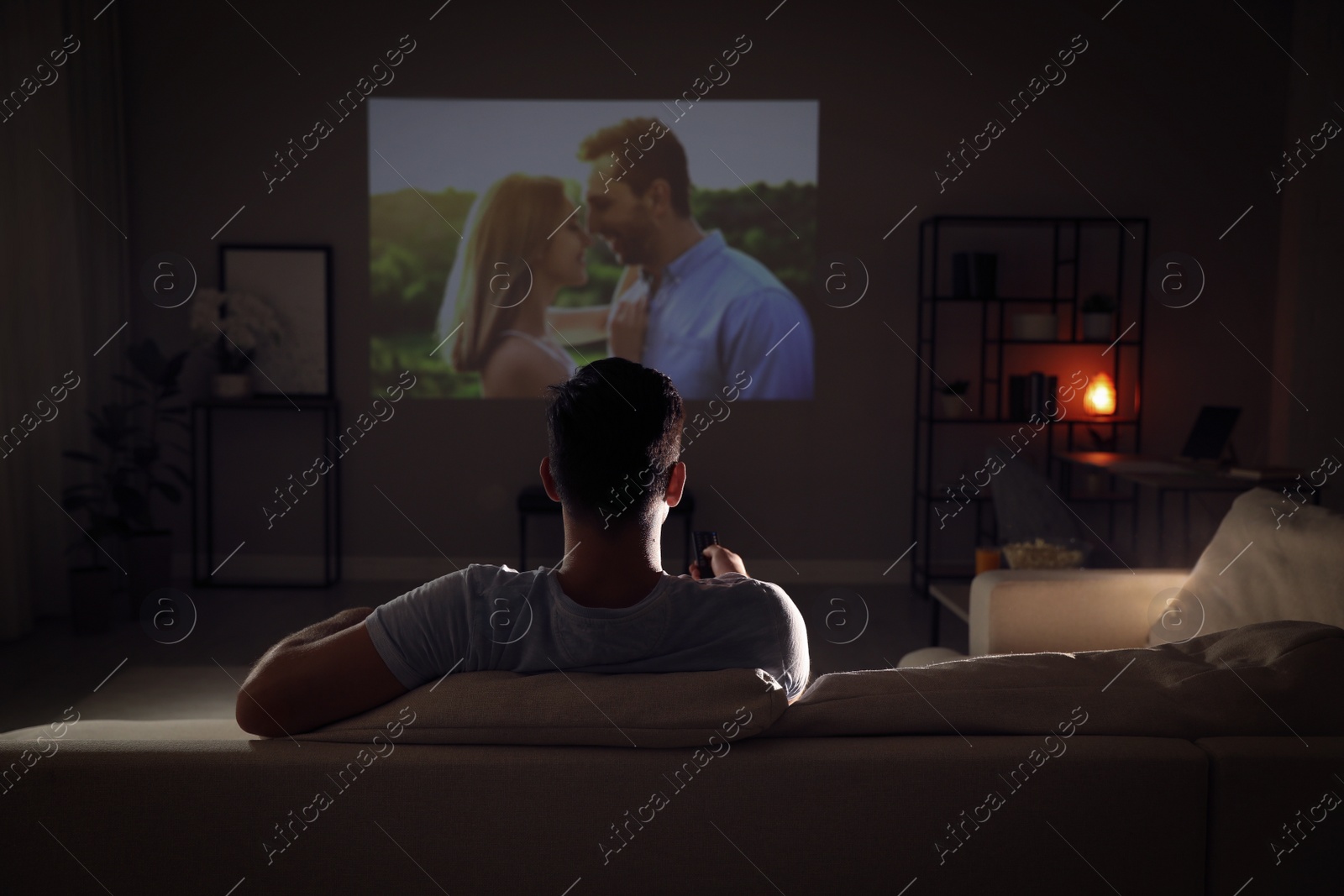Photo of Man watching movie on sofa at night, back view
