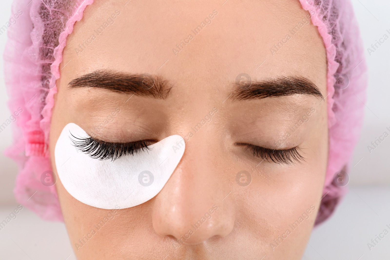 Photo of Young woman undergoing eyelash extensions procedure, closeup