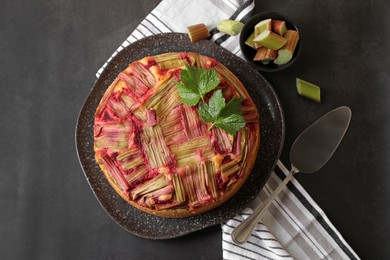 Photo of Freshly baked rhubarb pie, cut stalks and cake server on black table, flat lay