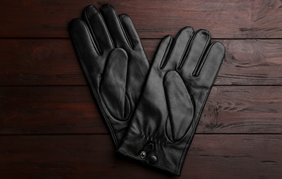 Stylish black leather gloves on wooden background, flat lay