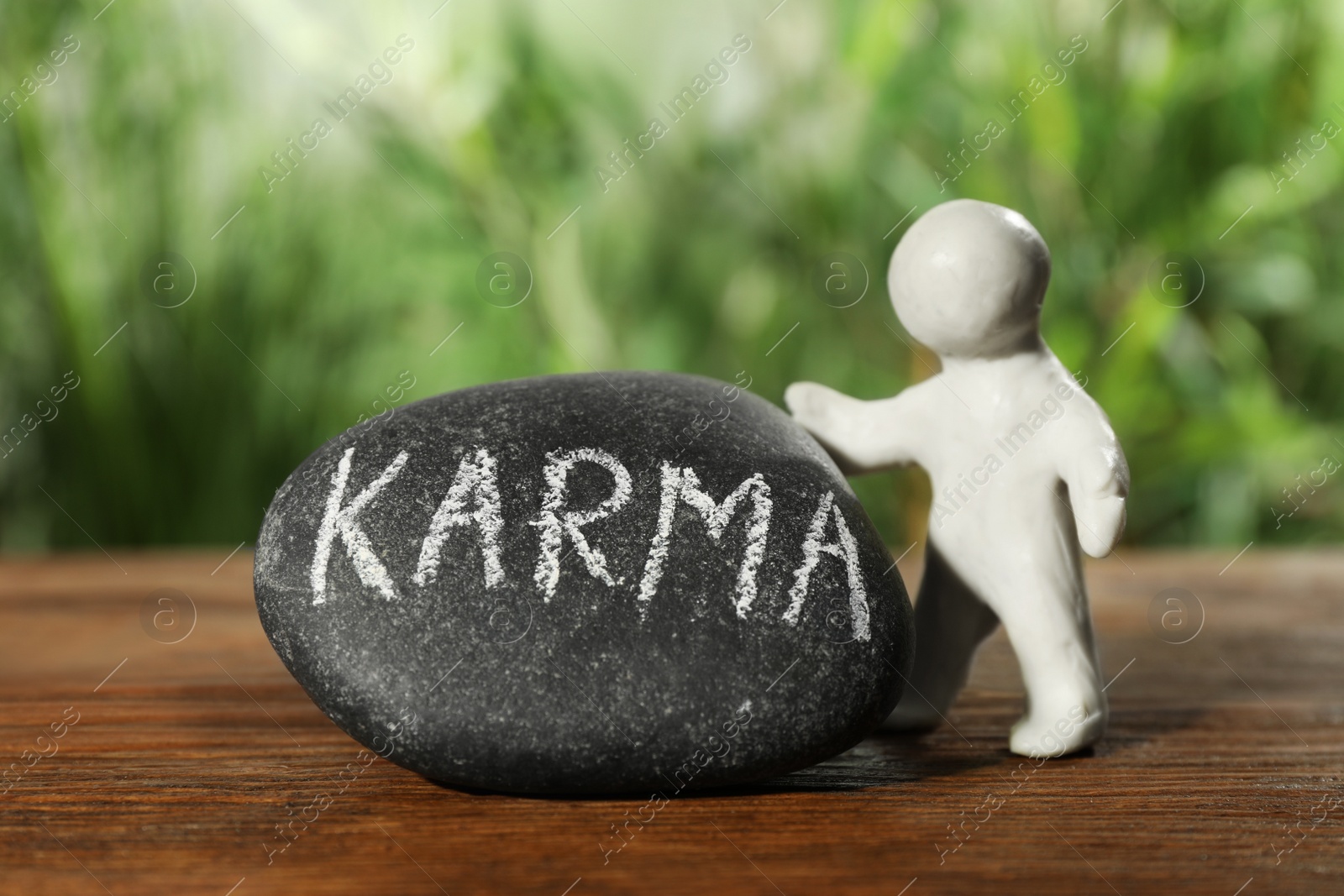 Photo of Human figure near stone with word Karma on wooden table, closeup