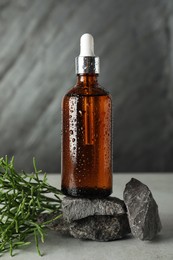 Photo of Bottle of hydrophilic oil, rocks and green plant on light grey table