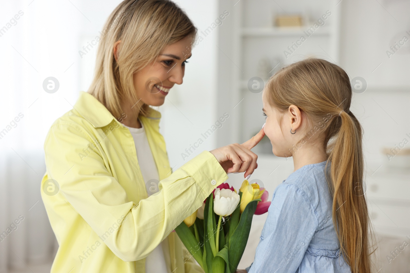 Photo of Little daughter congratulating her mom with bouquet of tulips at home. Happy Mother's Day