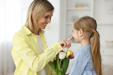 Little daughter congratulating her mom with bouquet of tulips at home. Happy Mother's Day