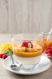 Delicious panna cotta with mango coulis, fresh fruit pieces and almond flakes on light wooden table