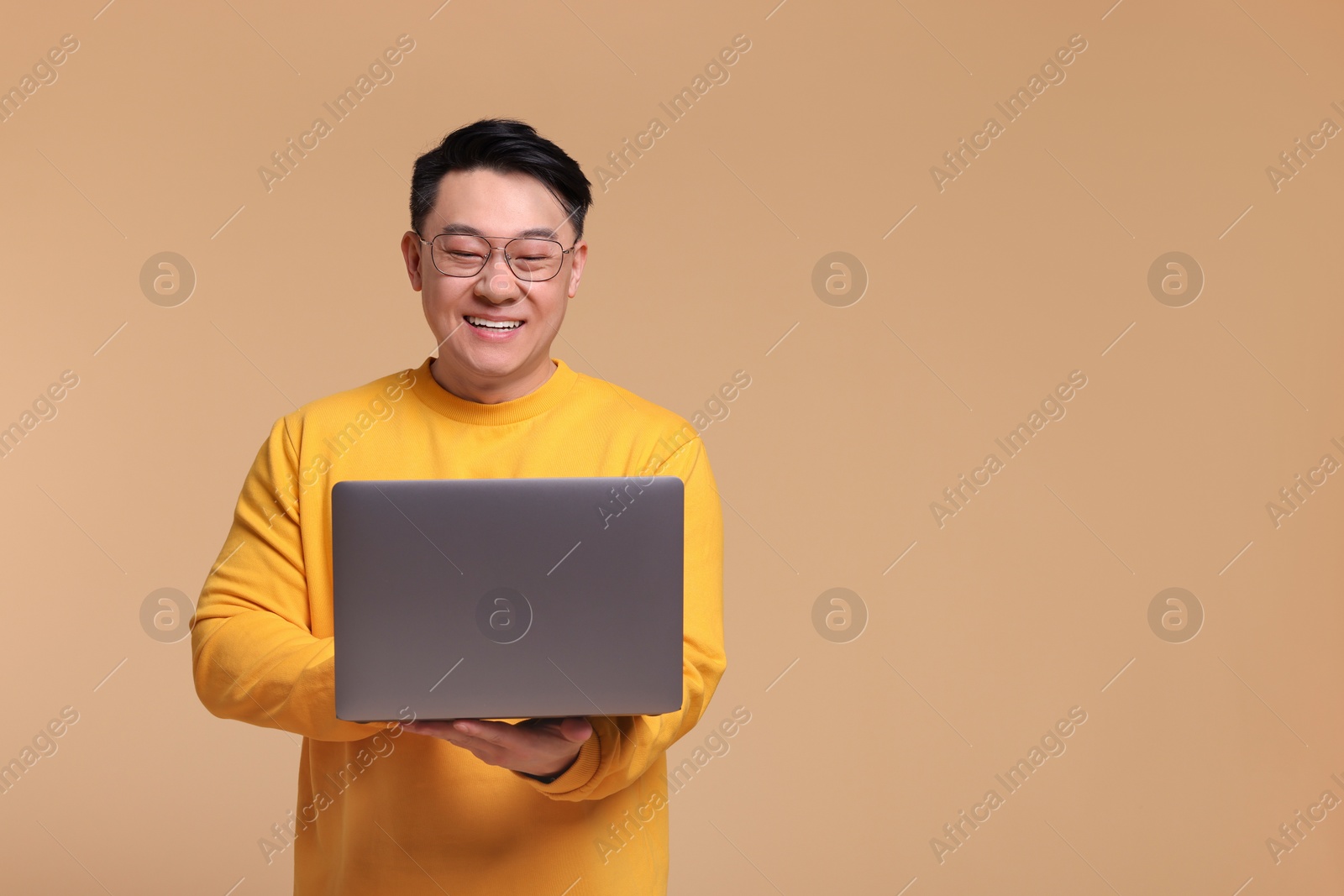 Photo of Happy man with laptop on beige background, space for text