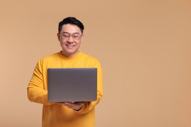 Happy man with laptop on beige background, space for text