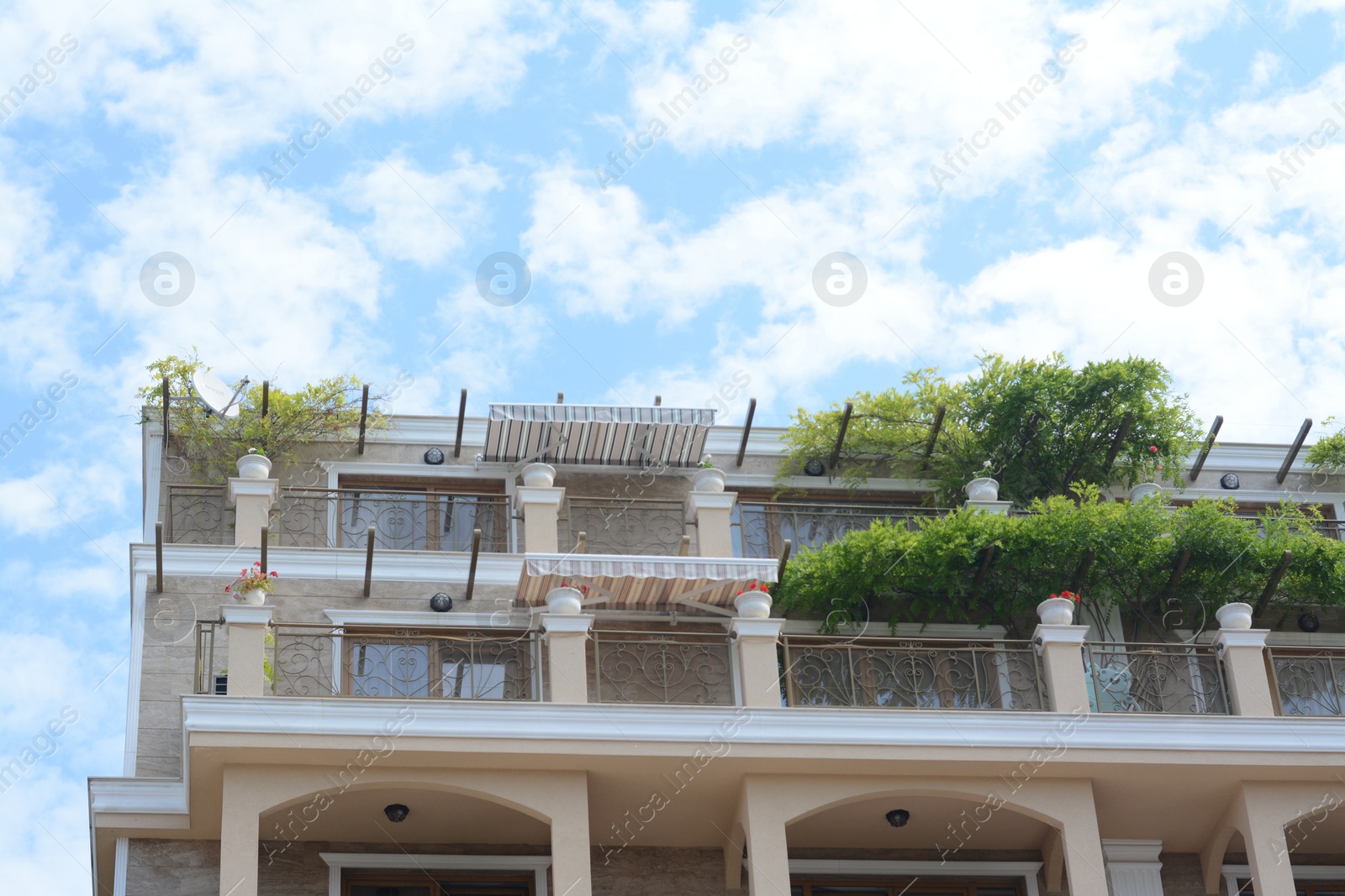 Photo of Exterior of beautiful building with balconies decorated with green plants against blue sky, low angle view