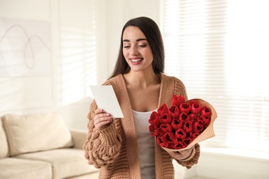 Happy woman with red tulip bouquet and greeting card at home. 8th of March celebration