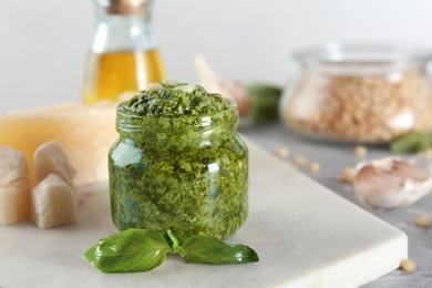 Photo of Board with jar of pesto sauce and basil on table. Space for text