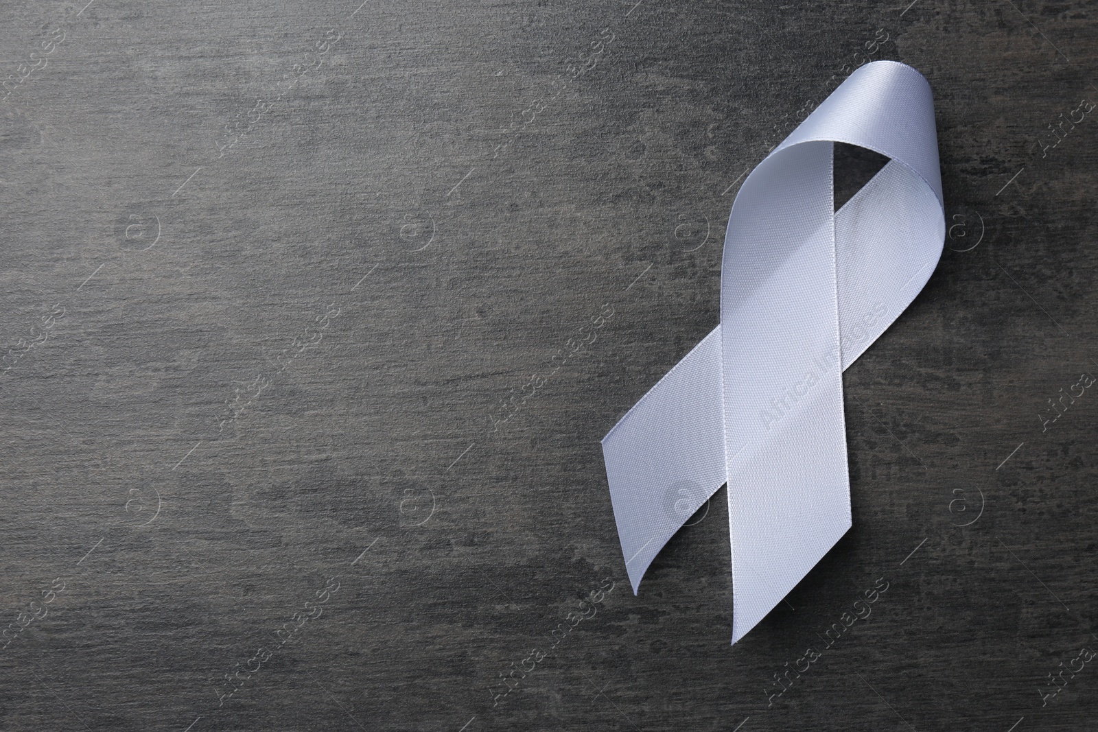 Photo of White awareness ribbon on grey table, top view. Space for text