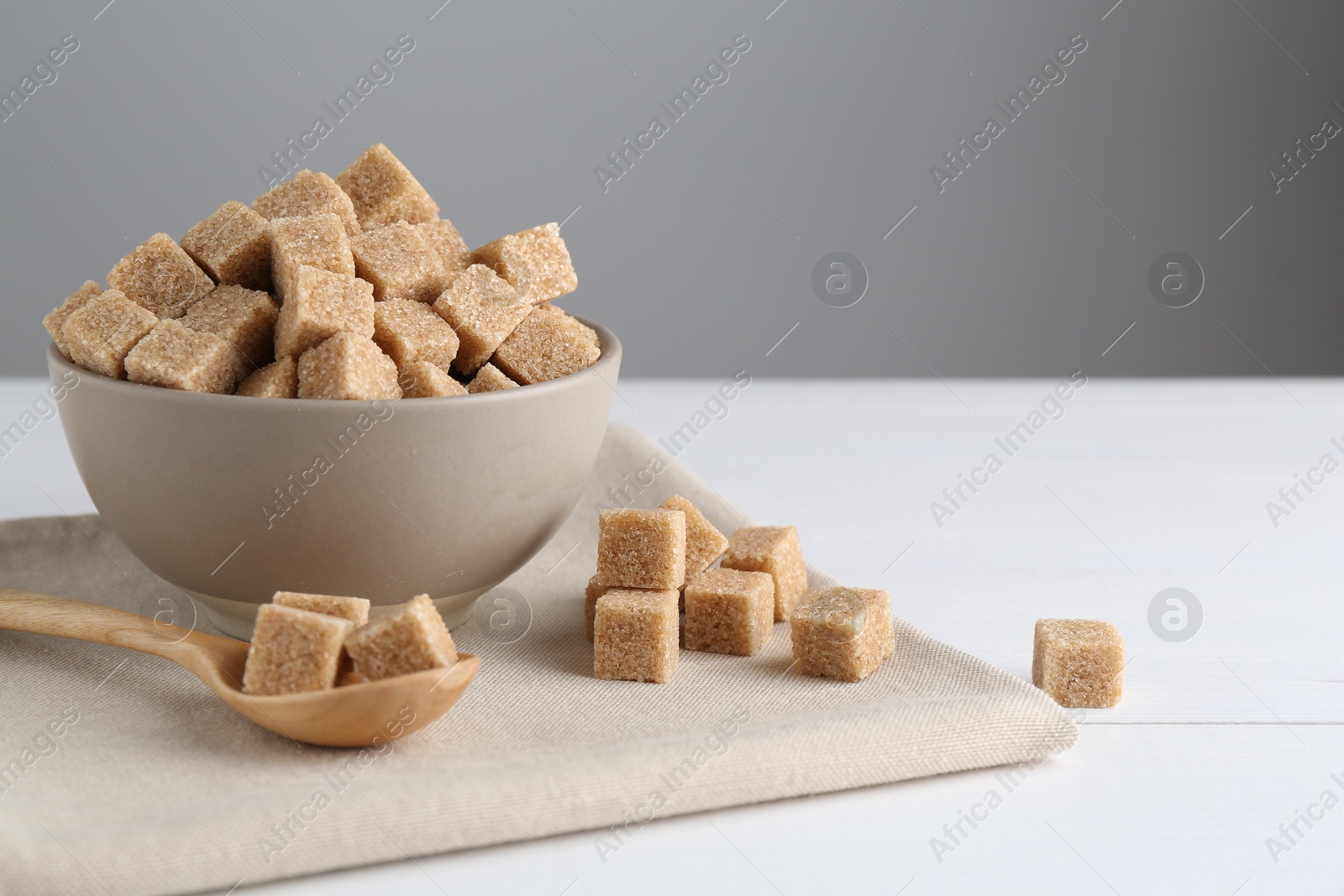 Photo of Brown sugar cubes on white wooden table, space for text