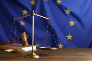 Photo of Scales of justice, judge's gavel and book on wooden table against European Union flag