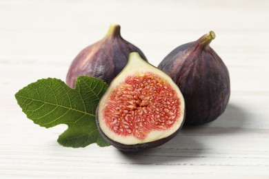 Photo of Whole and cut ripe figs with leaf on white wooden table, closeup