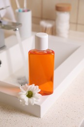 Photo of Fresh mouthwash in bottle and chamomile on sink in bathroom