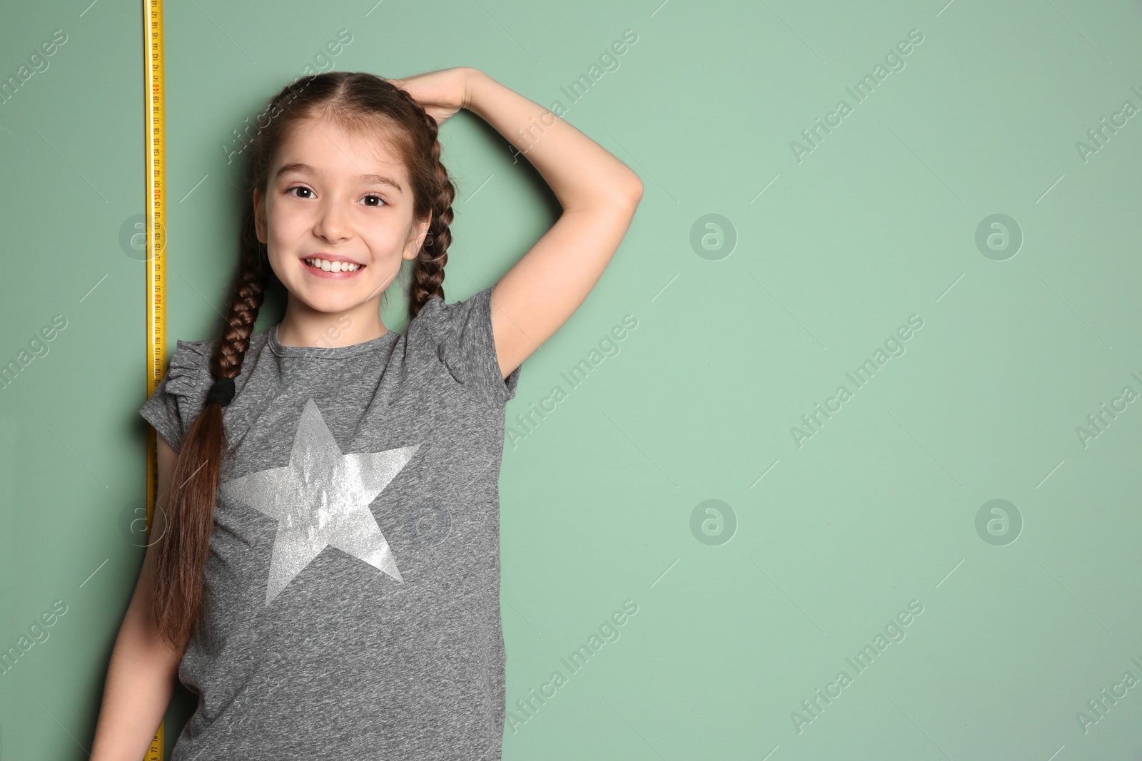 Photo of Little girl measuring her height on color background