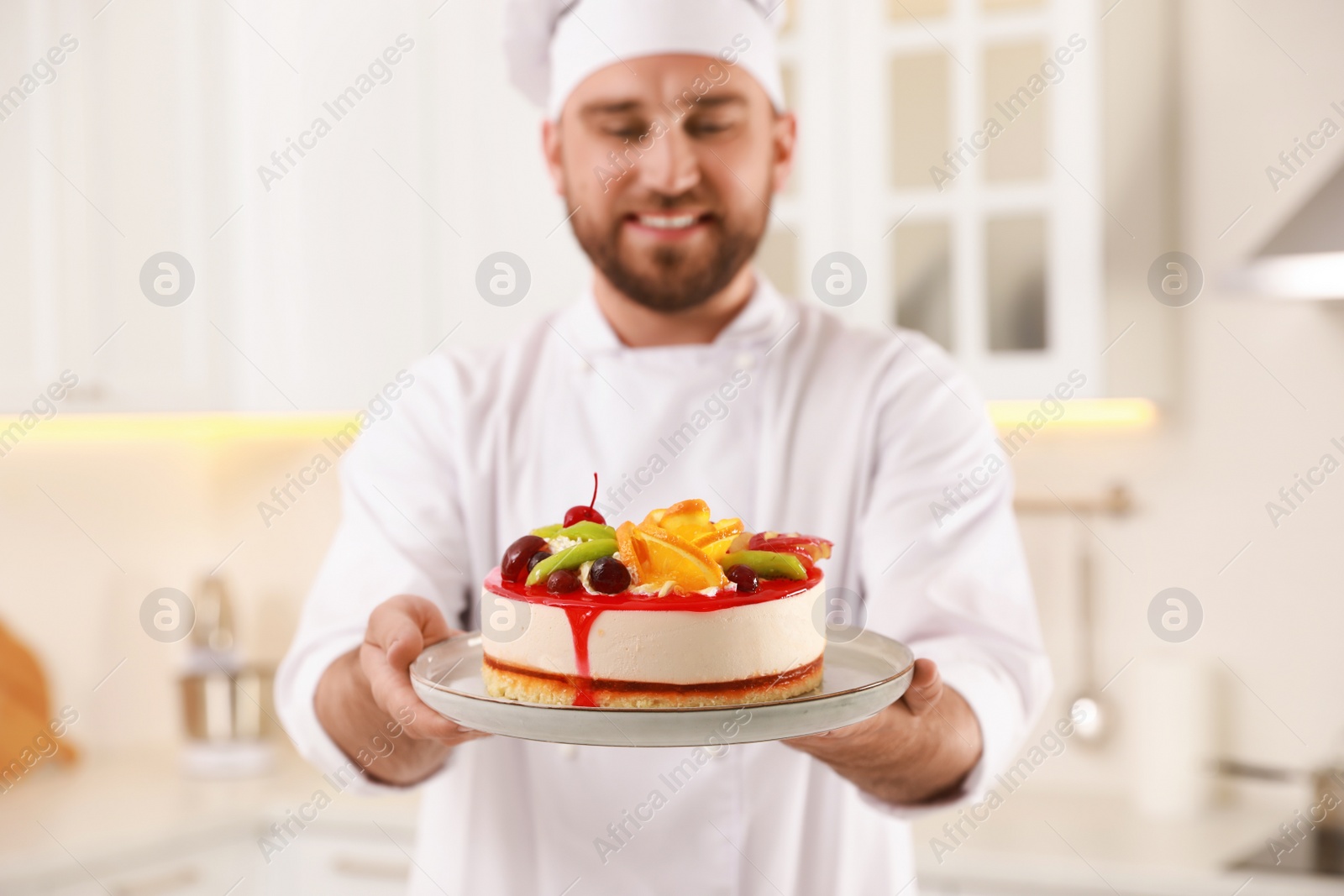 Photo of Happy professional confectioner holding delicious cake in kitchen, focus on hands